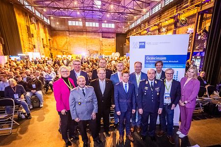 Gruppenfoto IT-Sicherheitstag vor dem IHK NRW Roll-up mit Publikum im Hintergrund.